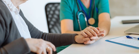 Healthcare professional holding the hands of an elder patient